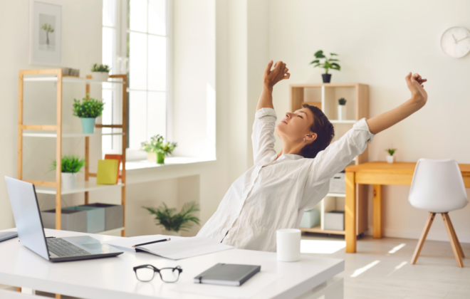 Woman stretching in front of laptop at her desk, choosing work-life balance